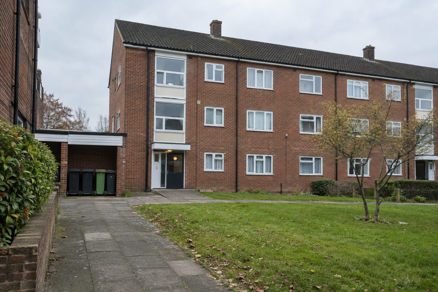 Red-brick social housing flats with communal entrances and wheelie bins, illustrating housing association regulation.